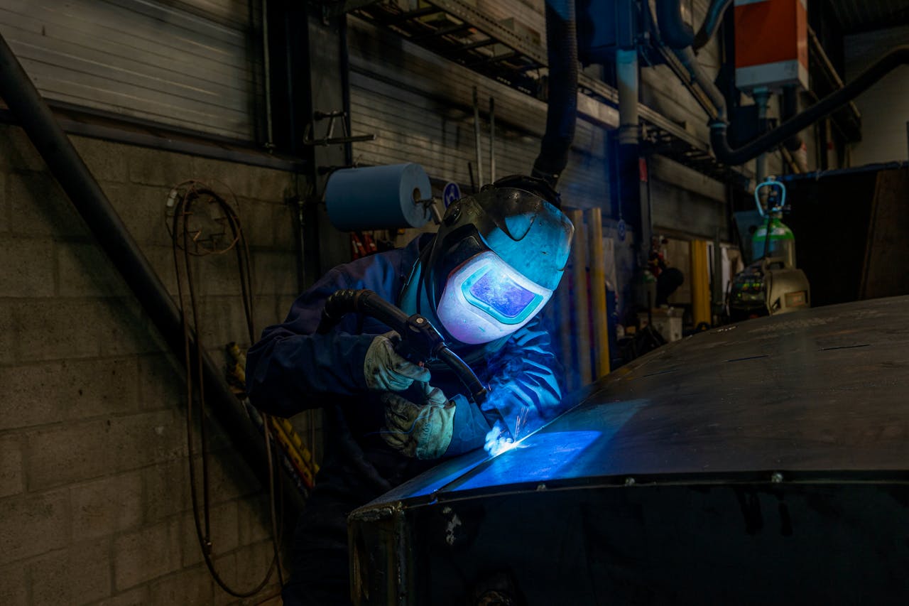 Welder wearing protective gear working in industrial workshop environment.