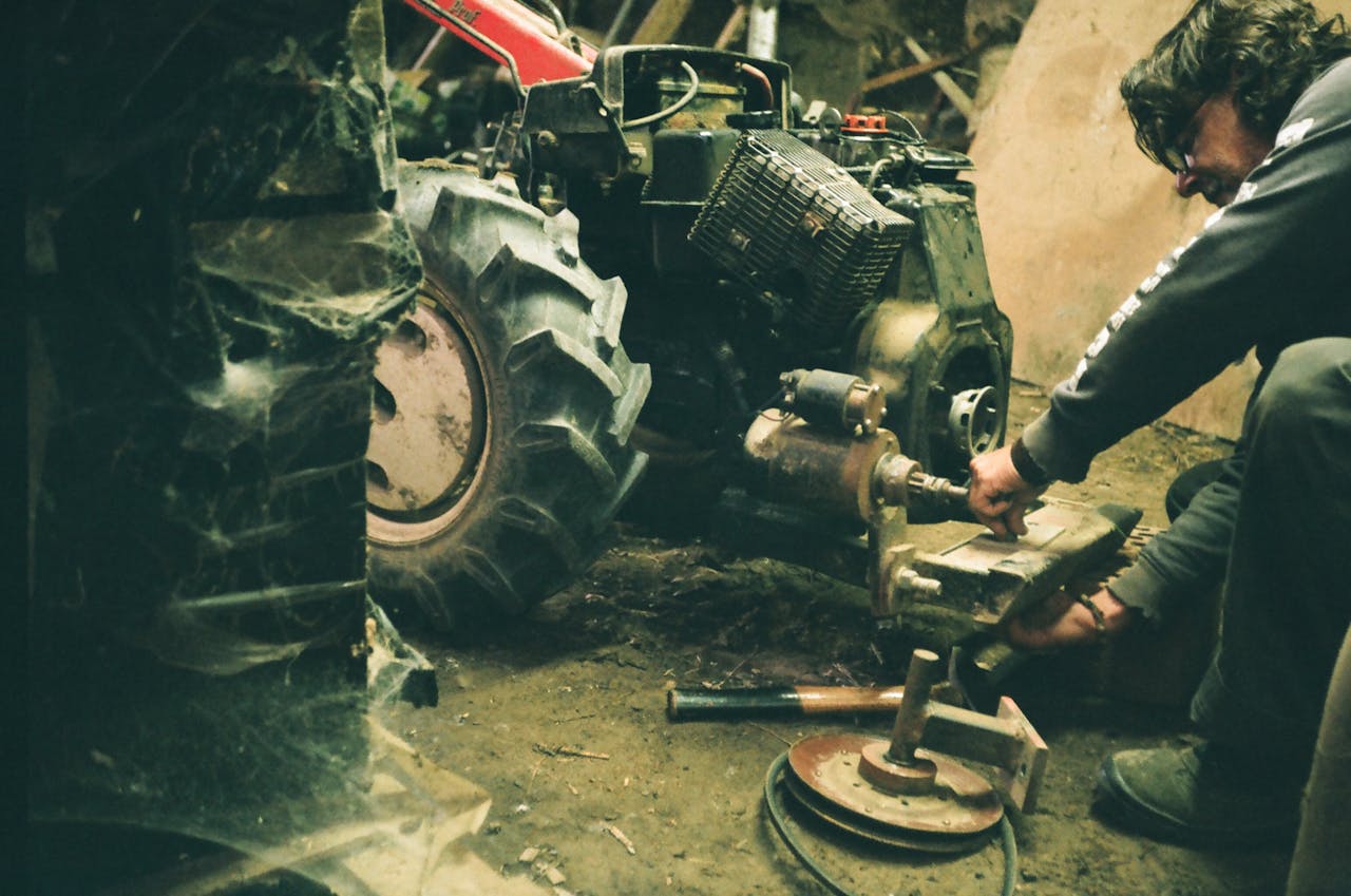 A mechanic working on a tractor's engine in a dimly lit indoor workshop.